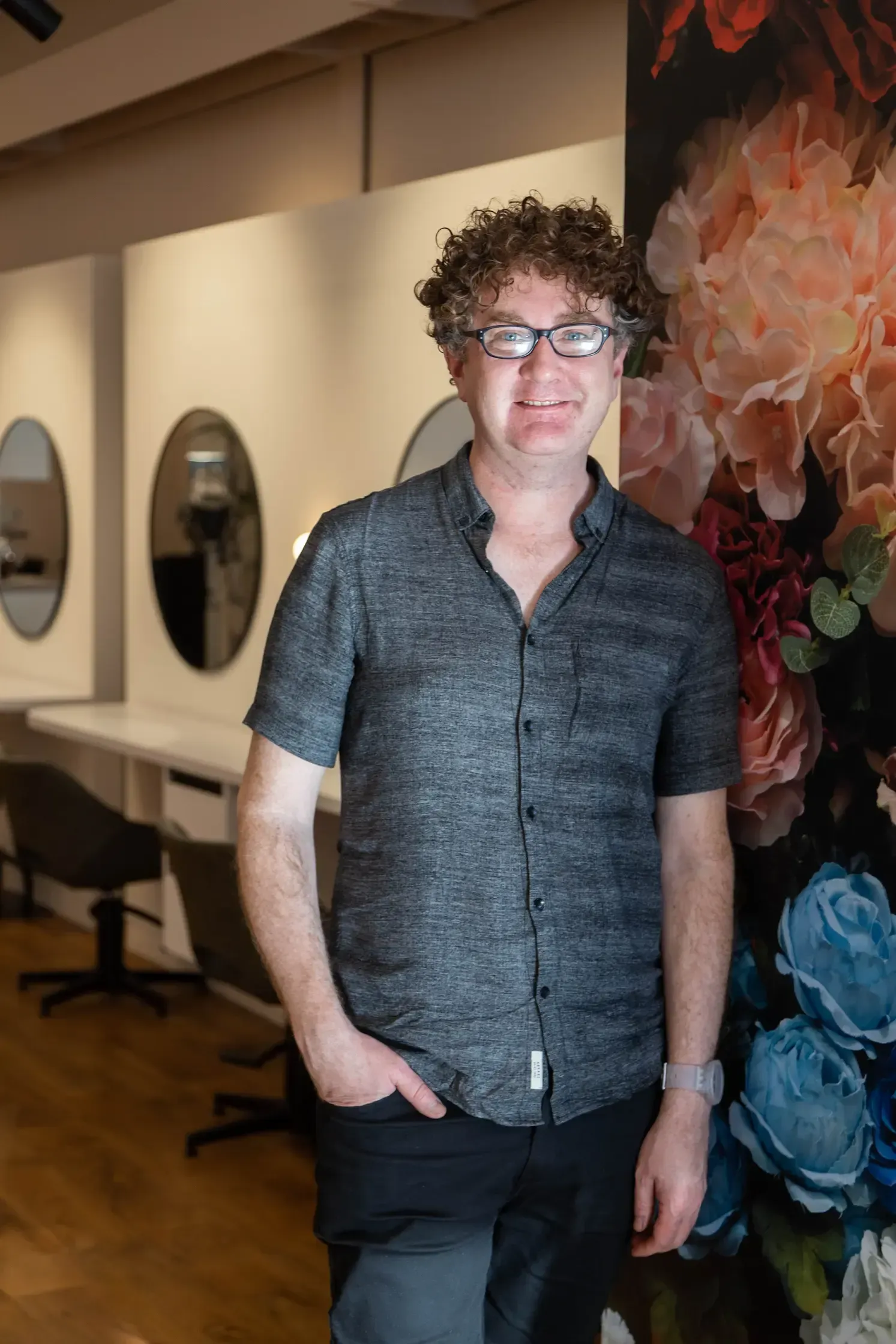 A man wearing glasses is sitting in front of a potted plant