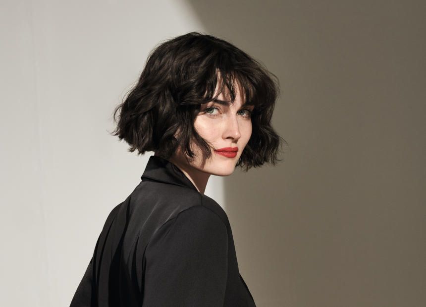 a woman with short hair is wearing a black jacket and red lipstick .