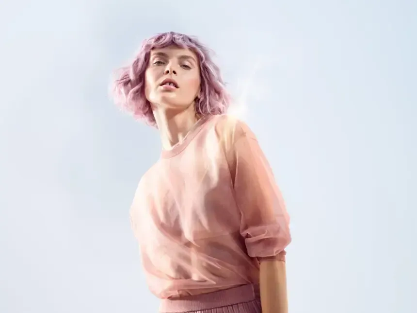 A woman with pink hair is wearing a pink sweater and a pink skirt.