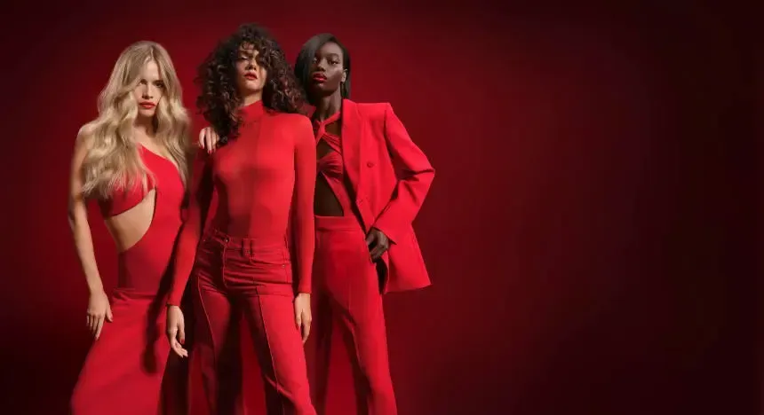 Three women in red dresses and suits are standing next to each other on a red background.