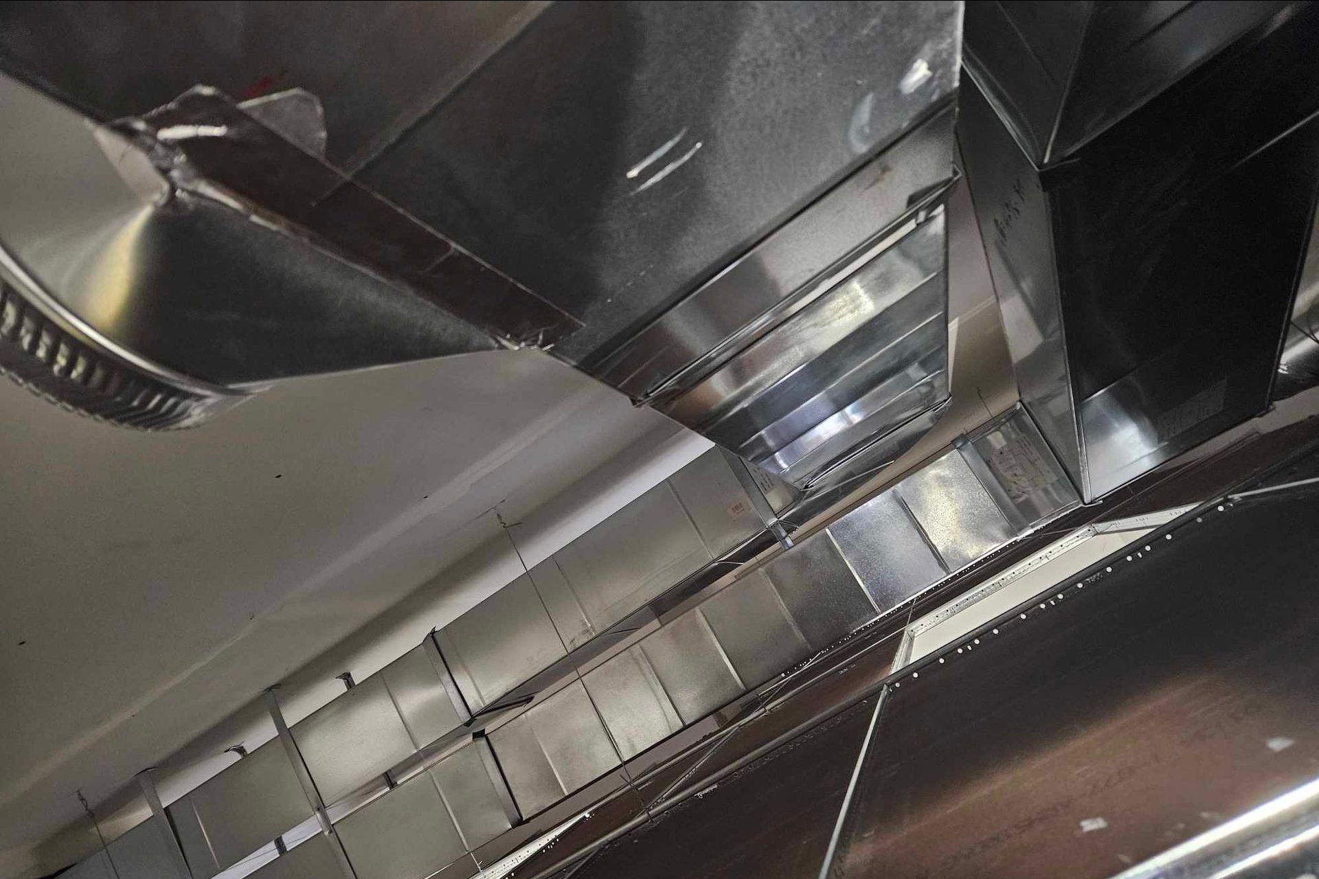 A stainless steel hood is hanging from the ceiling of a kitchen.