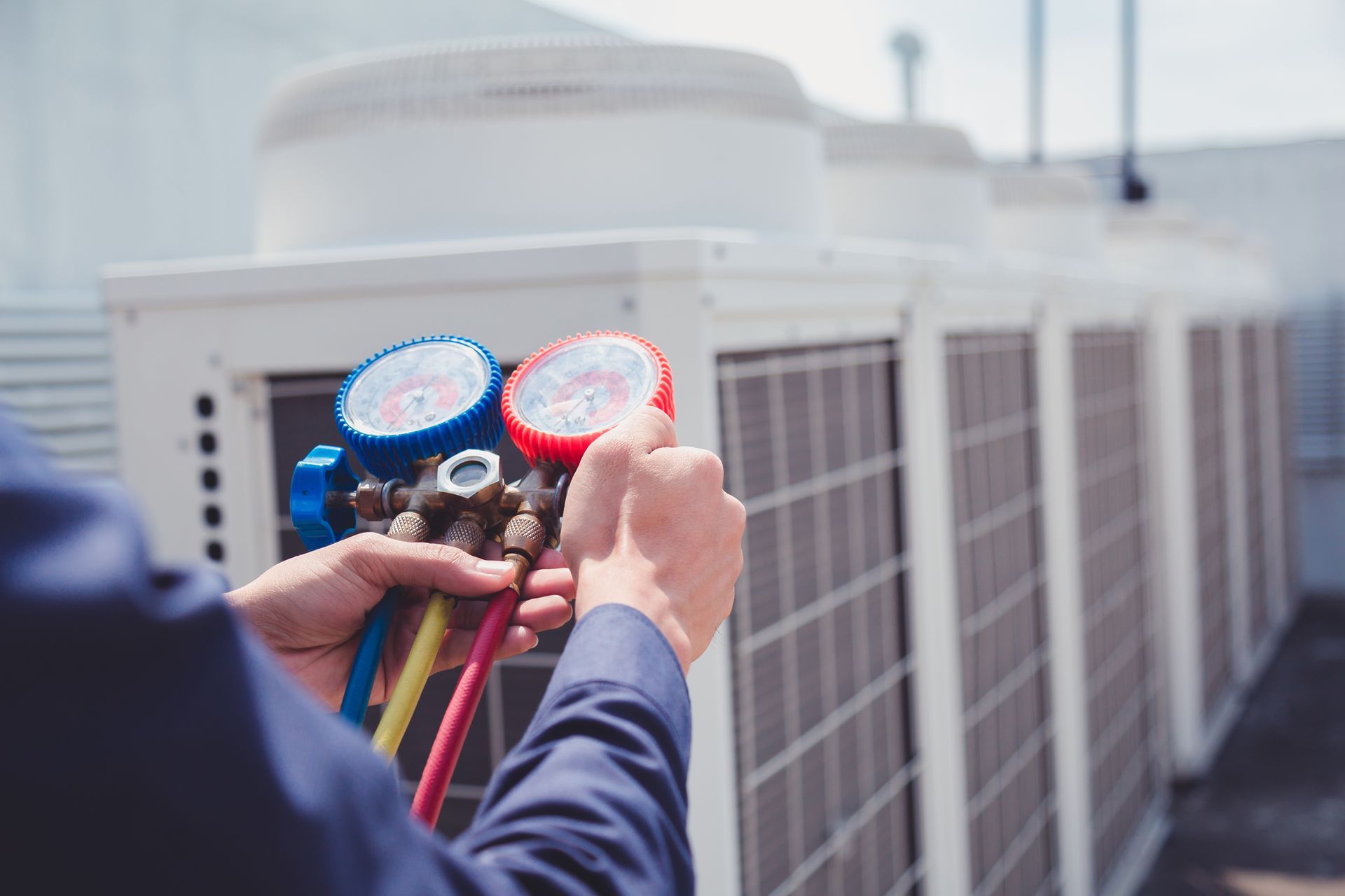 Technicien en CVC tenant des jauges, inspectant les unités de climatisation commerciales sur les toits.
