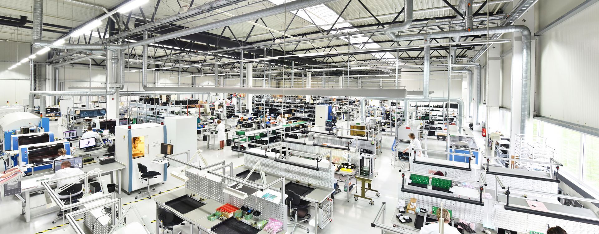 Grand intérieur d'usine moderne ; les machines et les postes de travail bordent le sol sous de hauts plafonds avec des conduits.