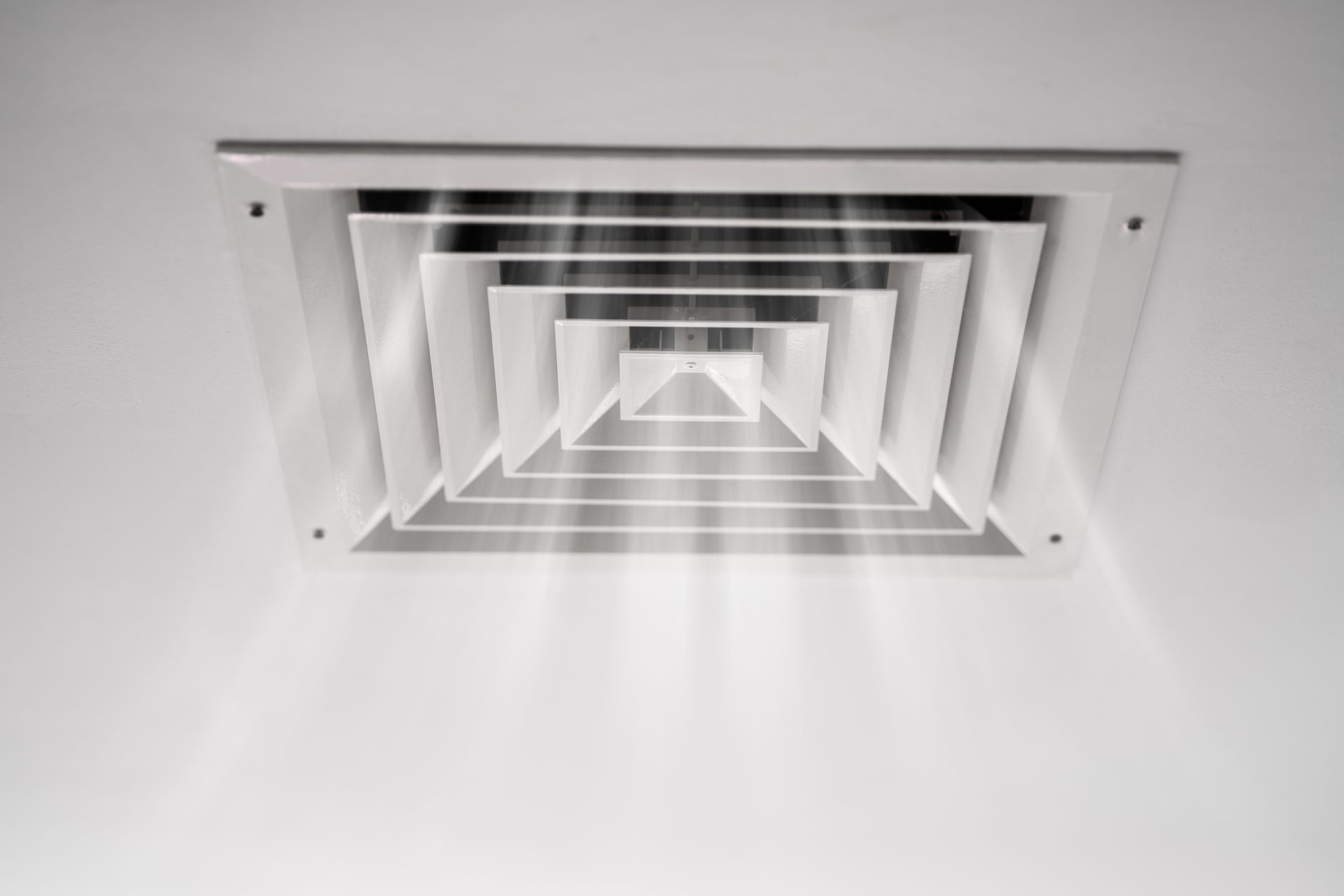 A close up of a square air vent on a white wall.