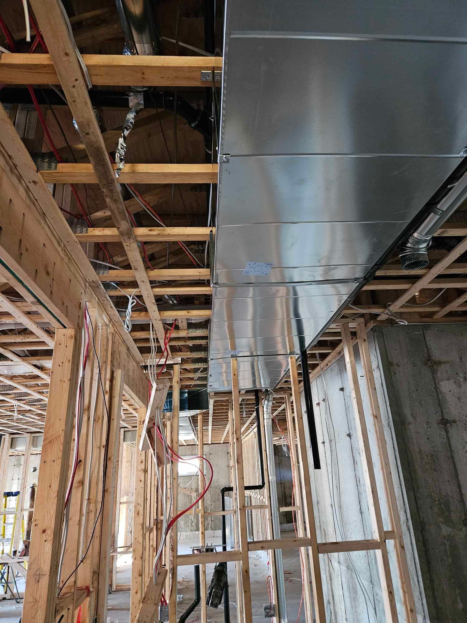 Un grand conduit métallique est suspendu au plafond d'un bâtiment en construction.