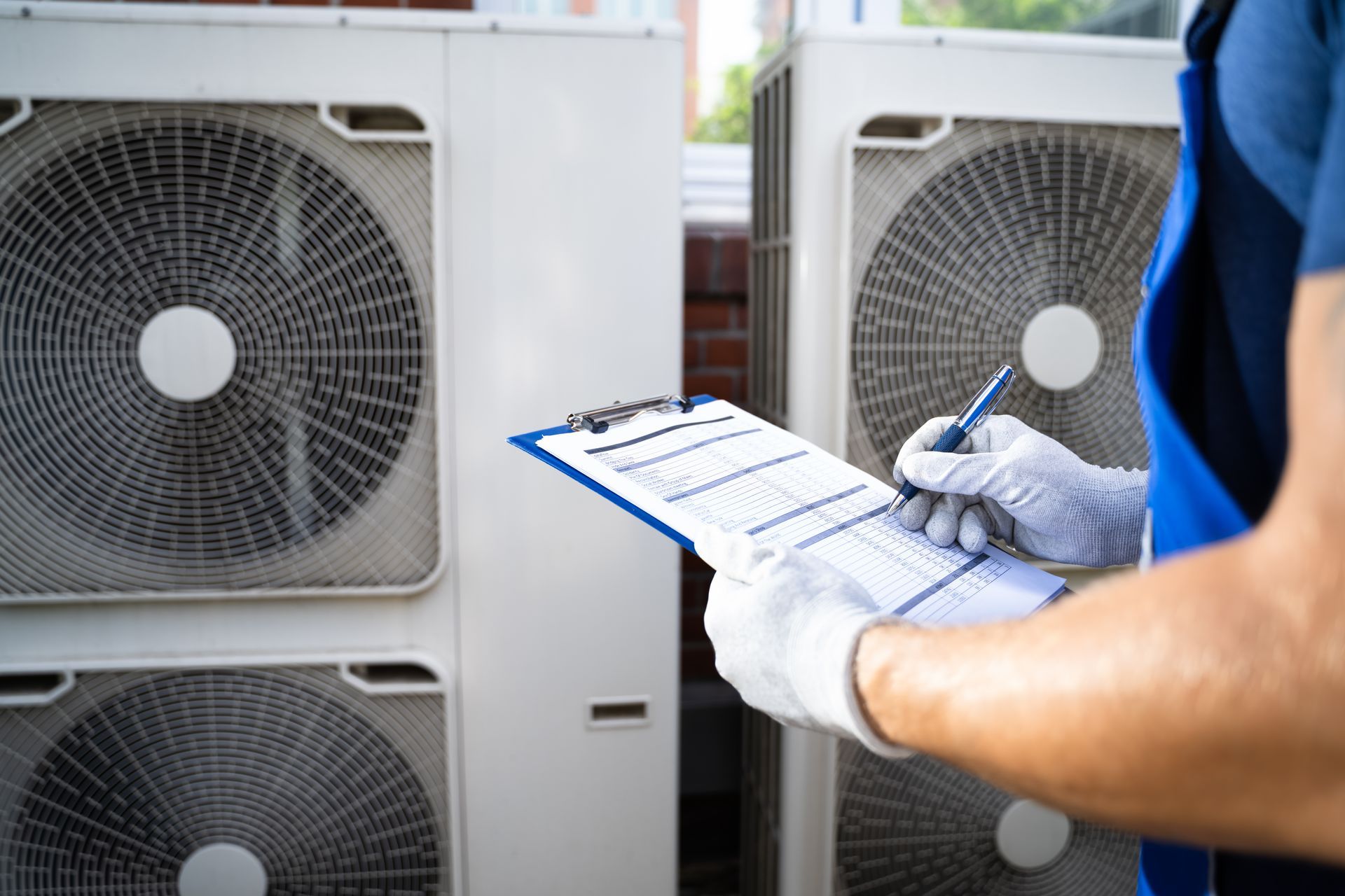 A man is writing on a clipboard in front of air conditioners.