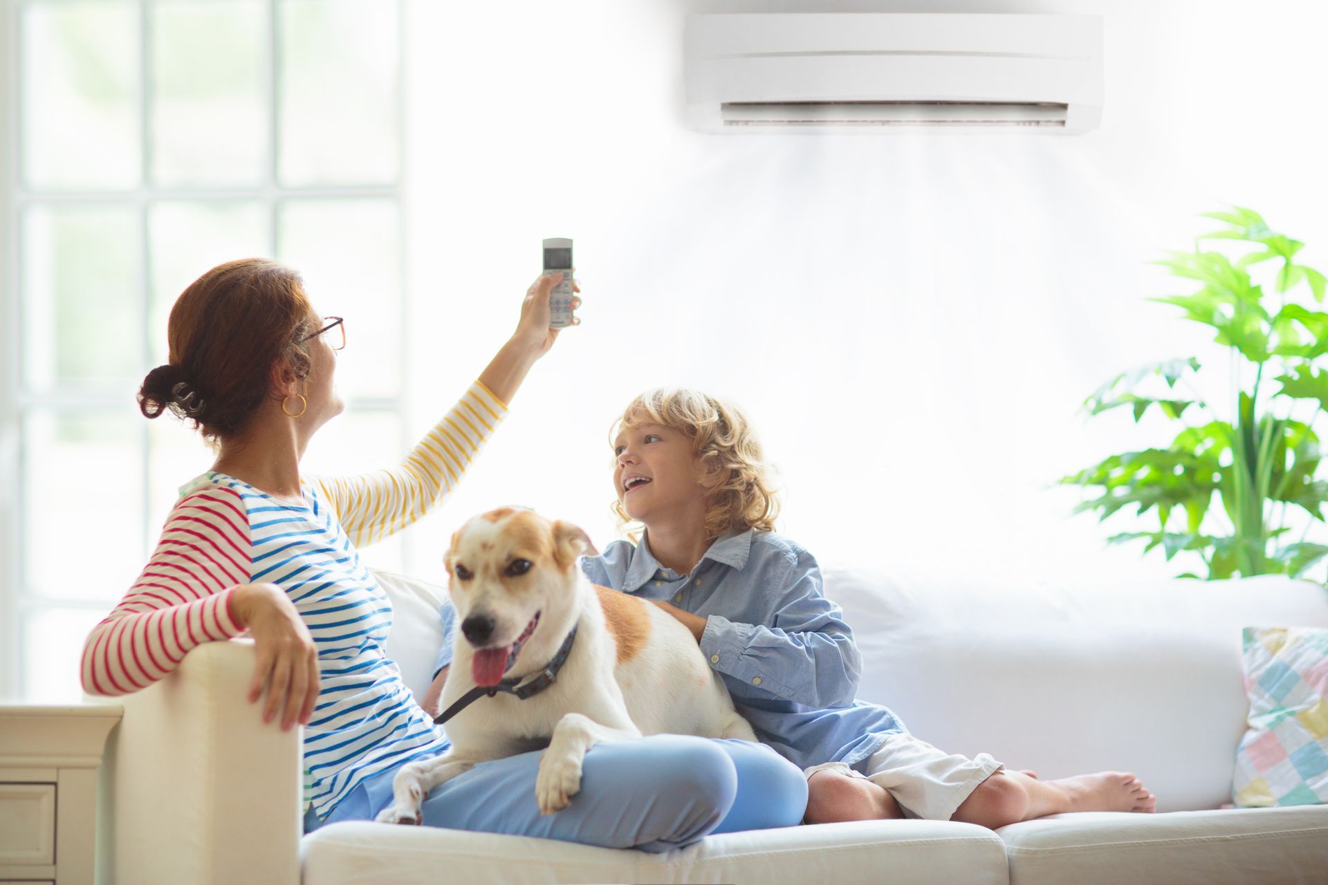 Une femme et un garçon sont assis sur un canapé avec un chien et une télécommande.
