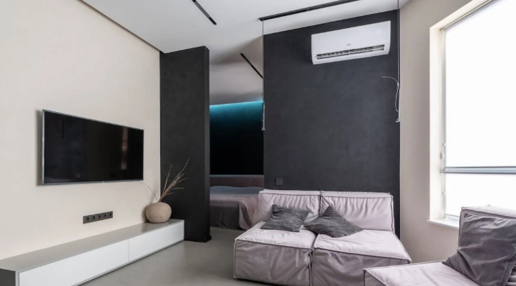 Salon moderne avec télévision, canapé et climatisation ; palette de couleurs neutres.