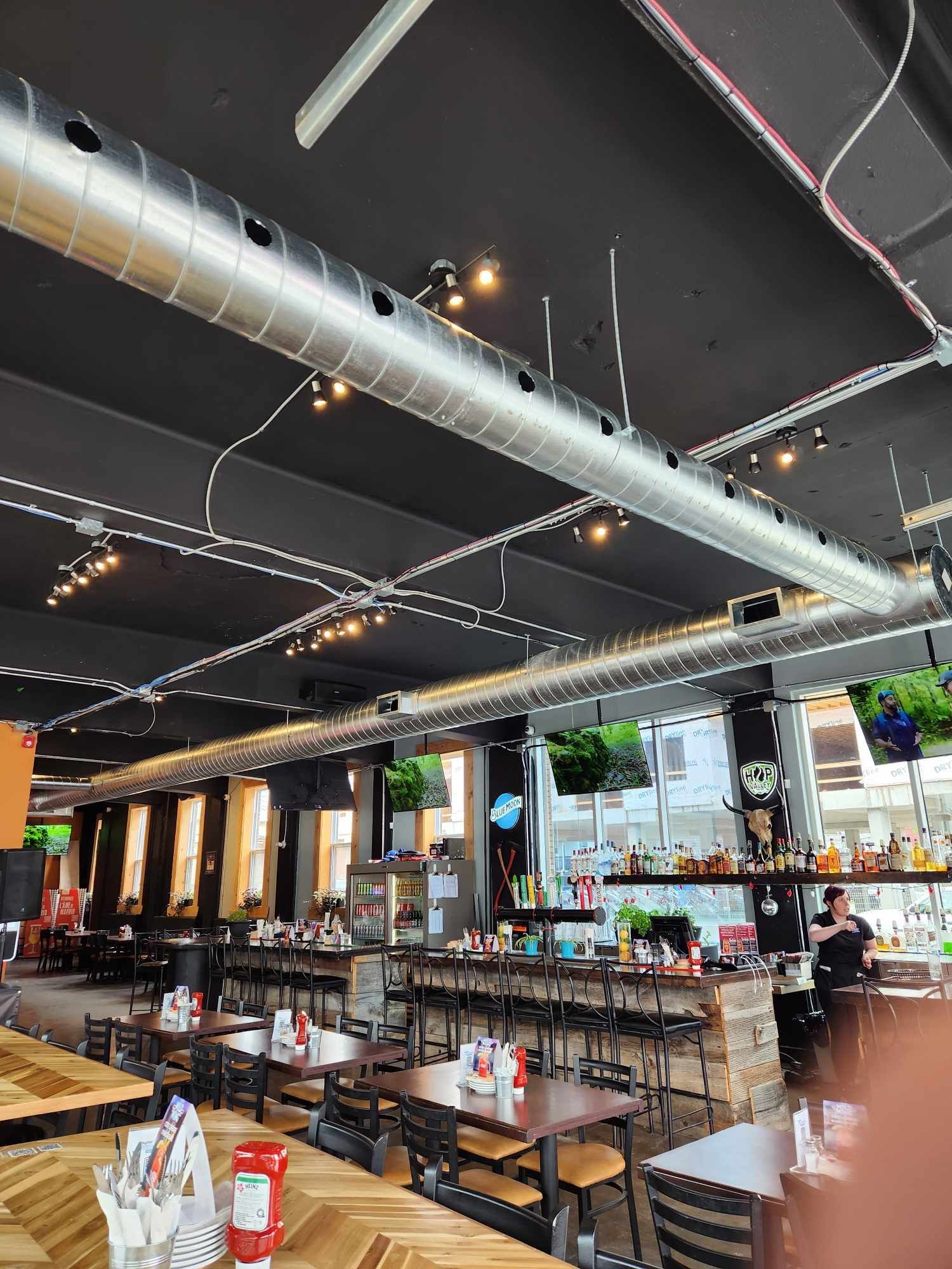 Intérieur d'un restaurant avec tables, bar et conduits métalliques. Des clients sont présents.