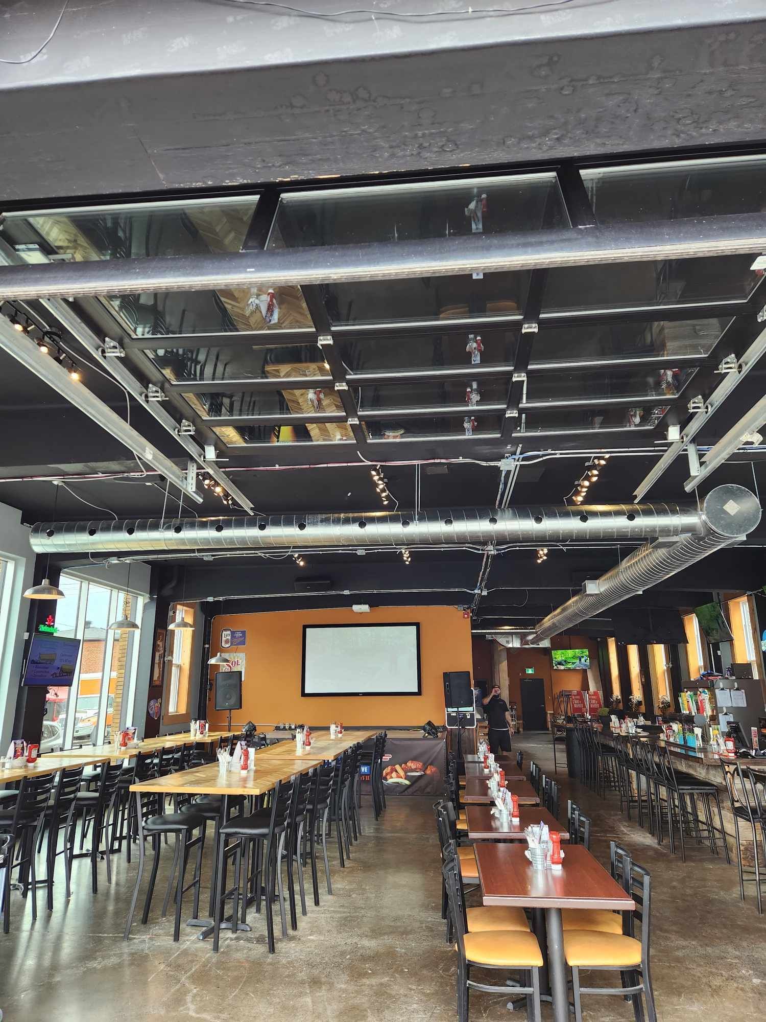 Intérieur d'un restaurant avec de longues tables, un écran de projection et un plafond noir.
