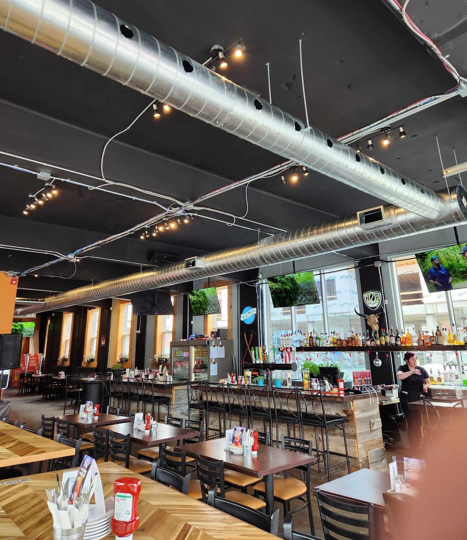 Intérieur d'un restaurant avec bar, tables et plafond noir laissant apparaître les conduits d'aération.