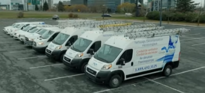 Des fourgons de service blancs sont garés en rang, avec des échelles sur le toit. Un bâtiment et le ciel se dessinent à l'arrière-plan.
