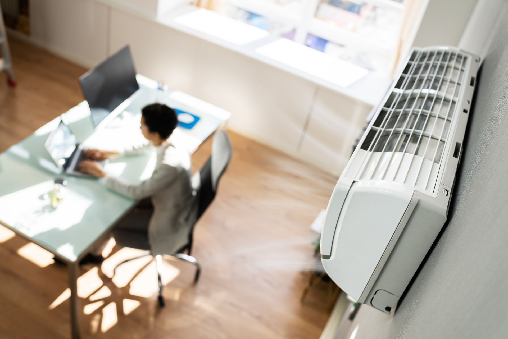 Un homme est assis à un bureau avec un ordinateur portable et un climatiseur.