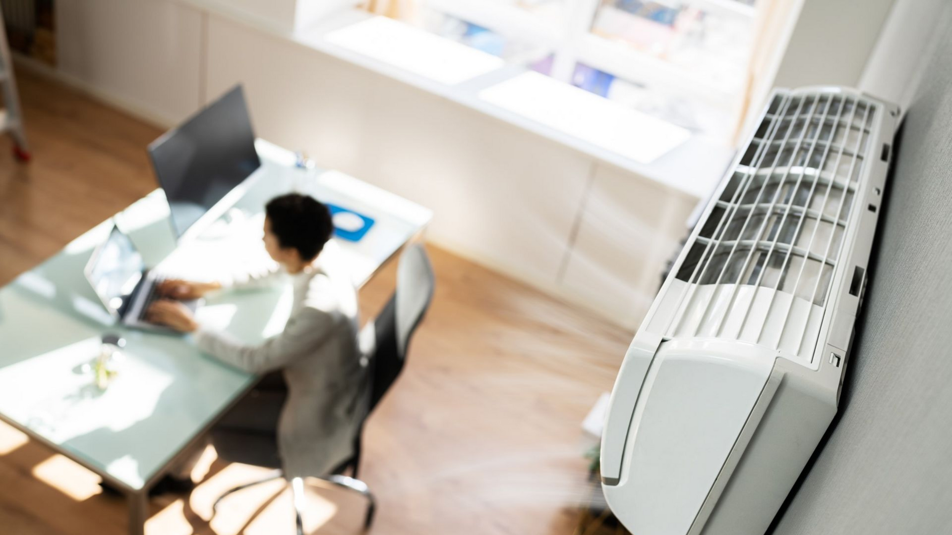 Un homme est assis à un bureau avec un ordinateur portable et un climatiseur.