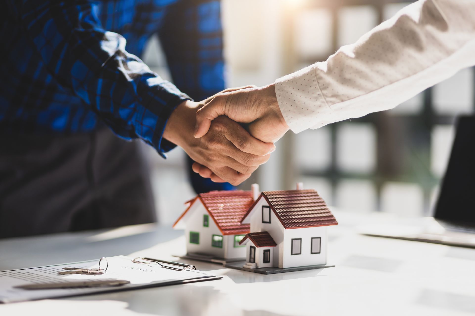 Handshake over a small house model, symbolizing a real estate agreement
