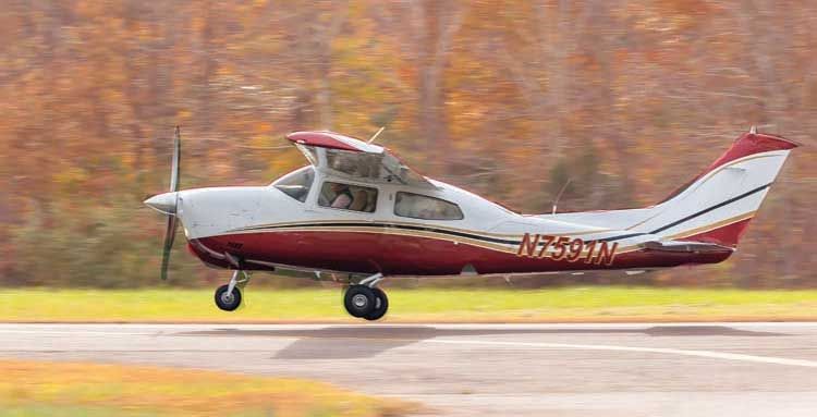 Small red-and-white airplane landing on a runway with autumn trees in the background