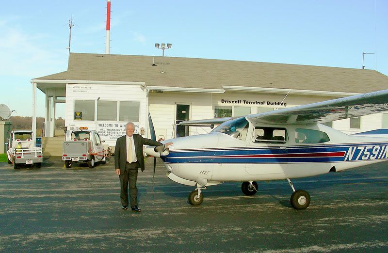 Man standing beside a small blue-and-white airplane in front of a hangar
