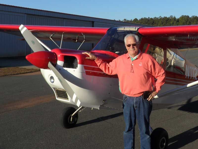 Man standing beside a red-and-white single-engine airplane on a runway