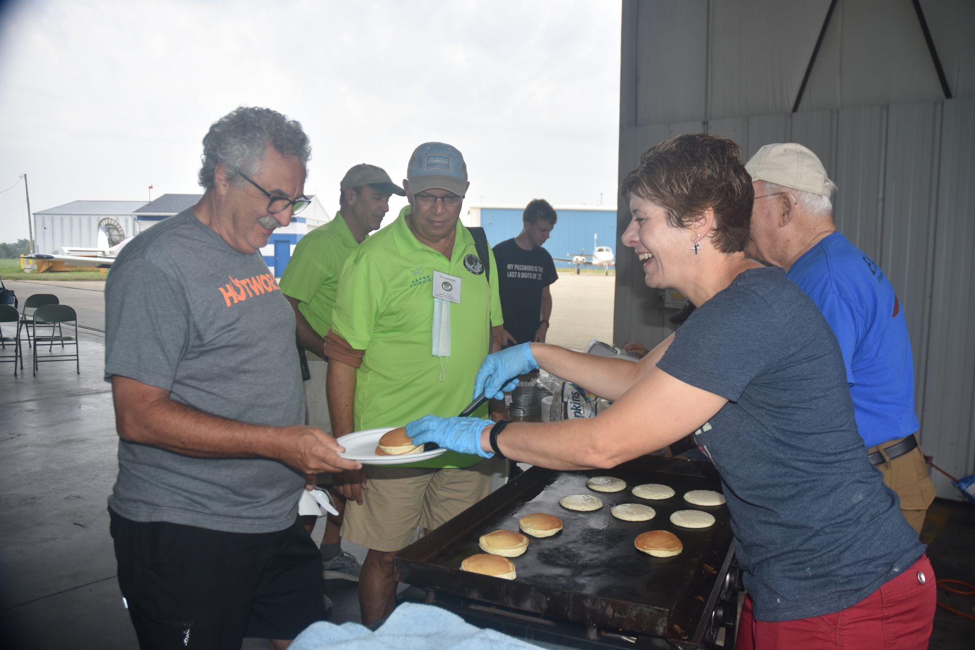 People serving grilled burgers at a food stall under a tent