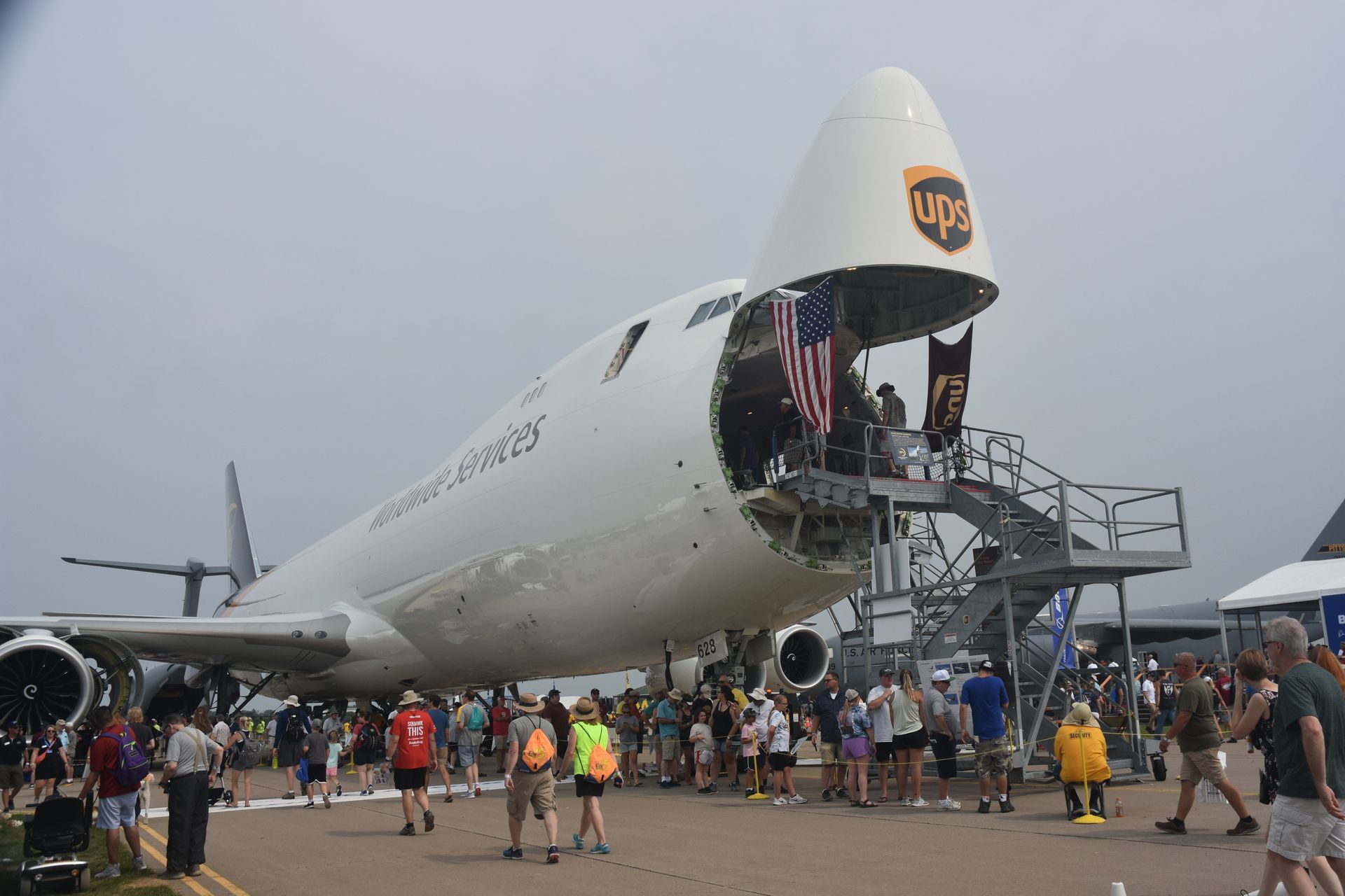 A large UPS cargo plane with its nose door open at an outdoor airshow, surrounded by a crowd of people.