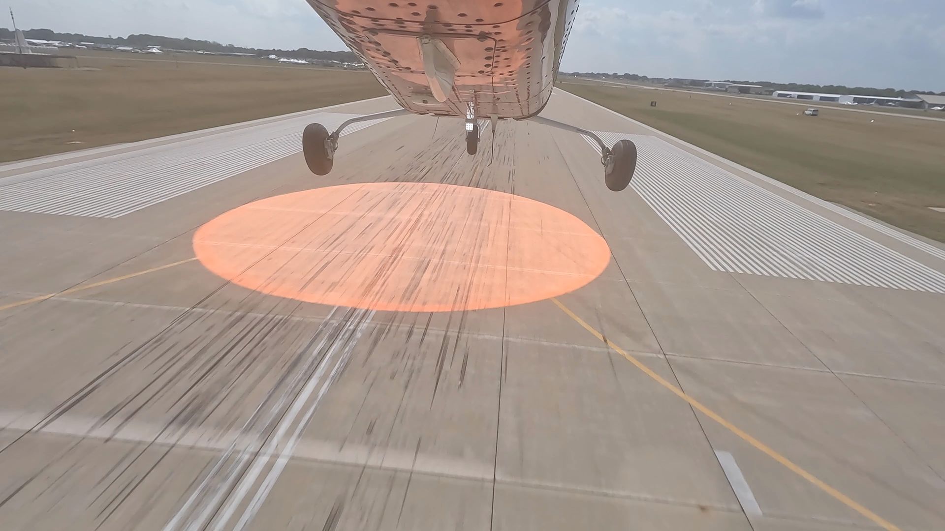 Airplane landing view over runway with a large orange circular marking and visible landing gear.