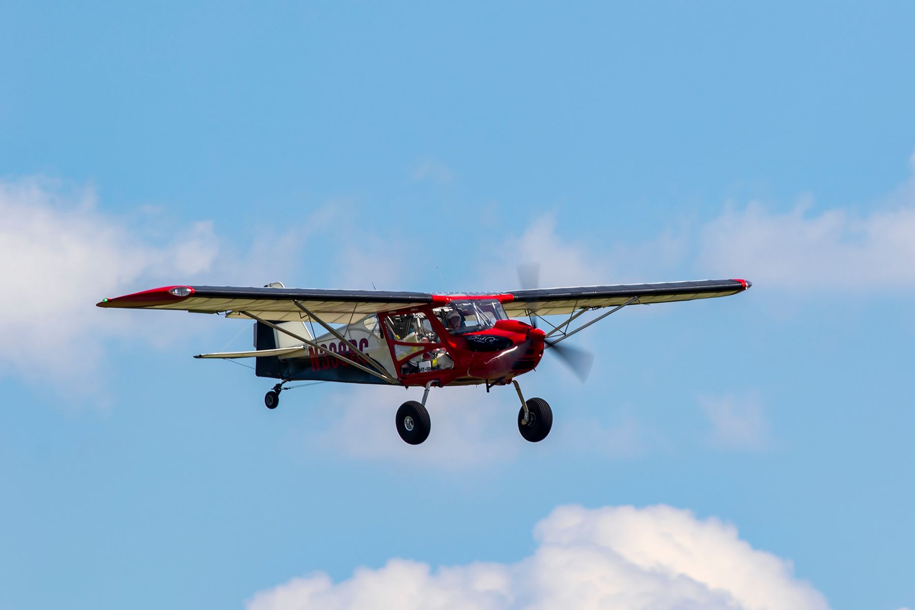 Red and white small airplane flying in a blue sky with clouds