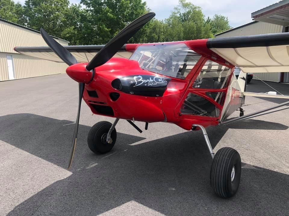A bright red, single-engine bush plane parked on an asphalt ramp in front of hangars.