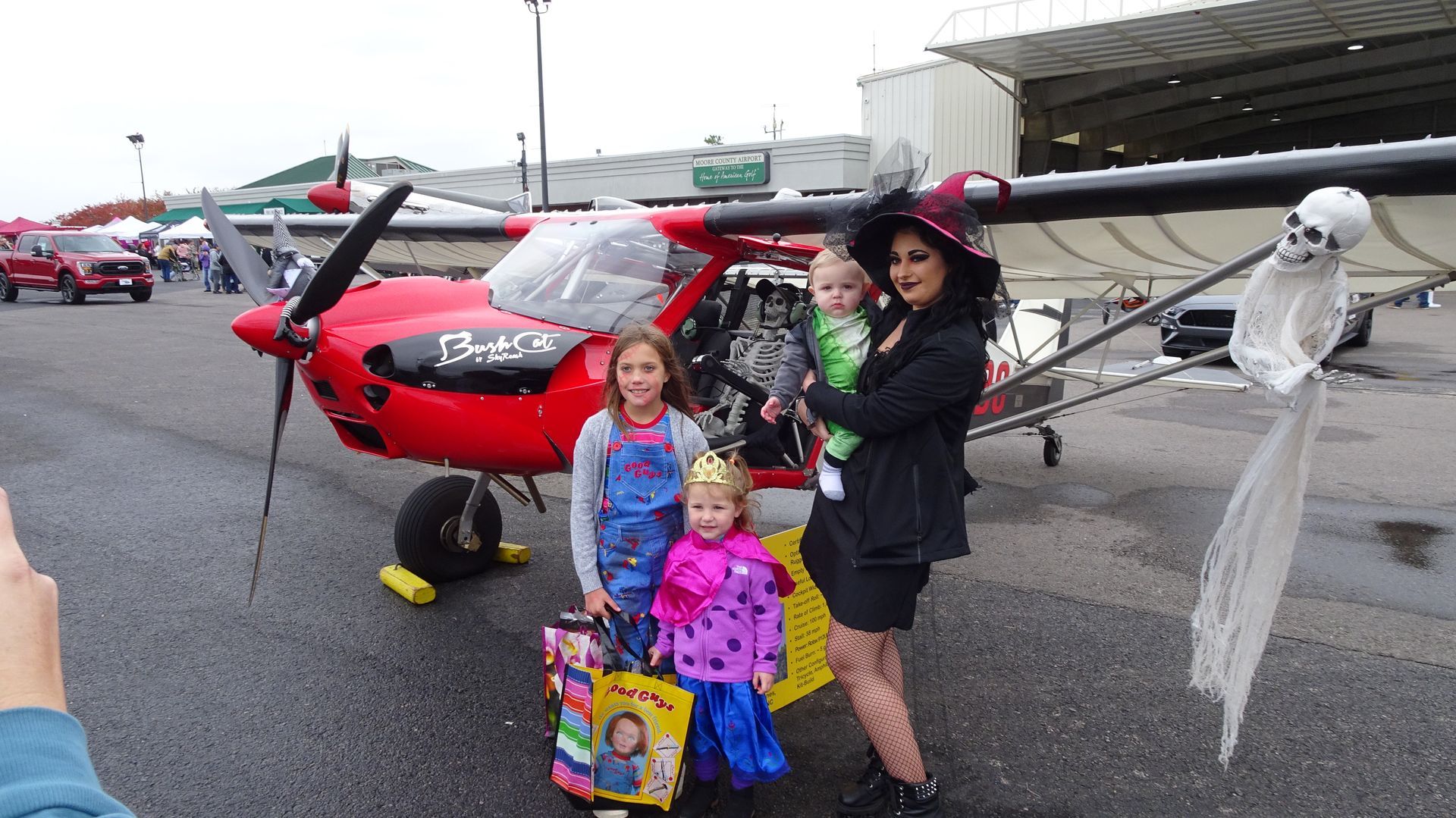 A person and three children in Halloween costumes pose in front of a red, propeller-driven plane decorated with a ghost.