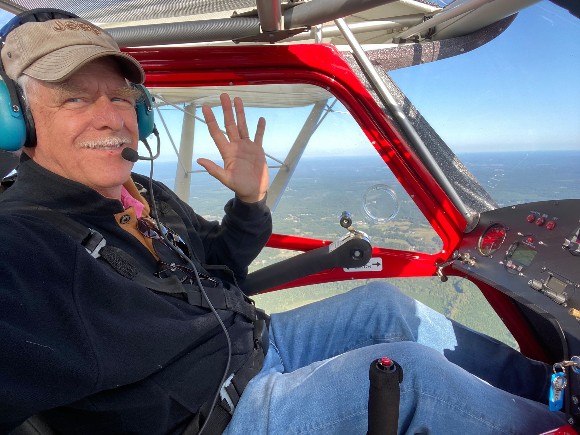 Man waving from a red aircraft cockpit with a mountain view outside the window