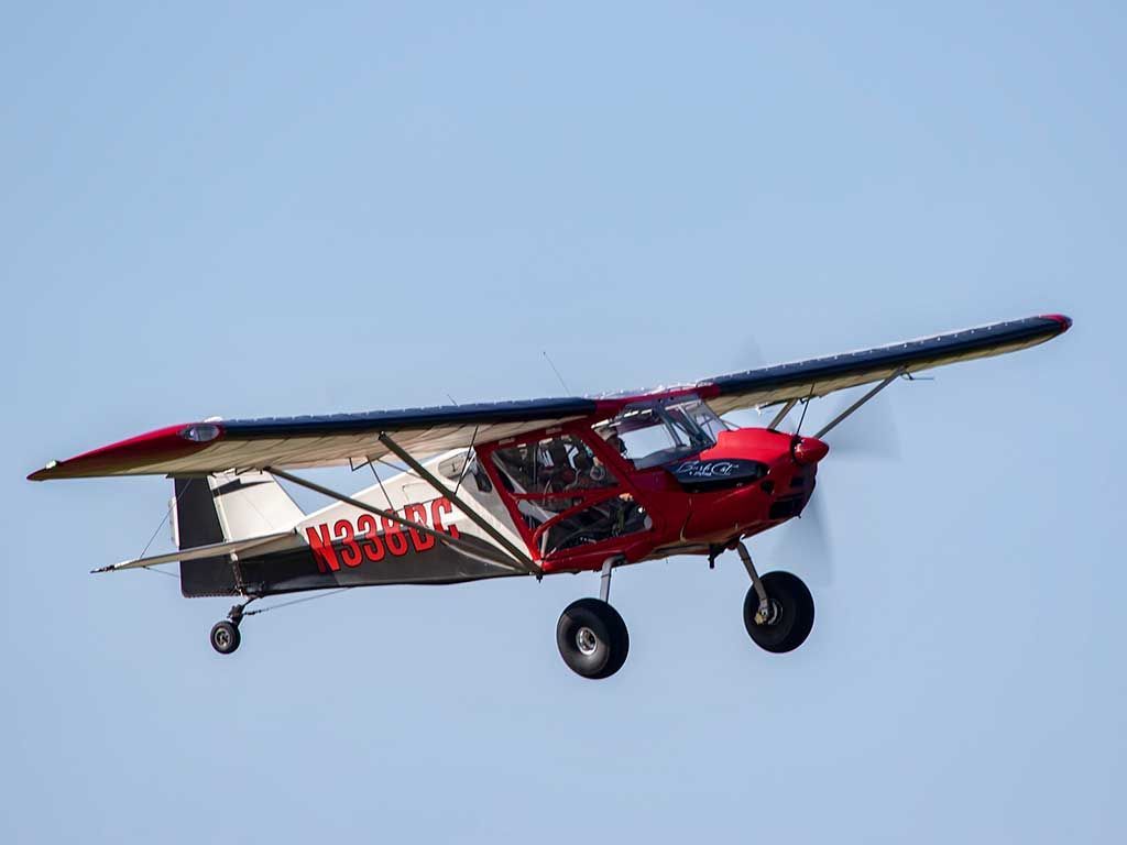A red and white bush plane with large tundra tires flying against a clear blue sky.