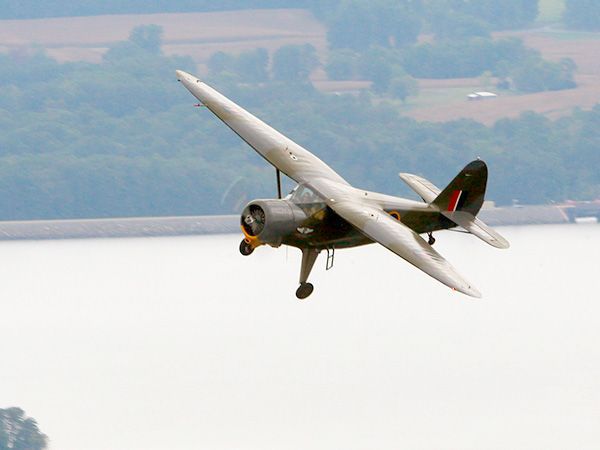 Vintage biplane banking over a calm river with a blurred shoreline in the background