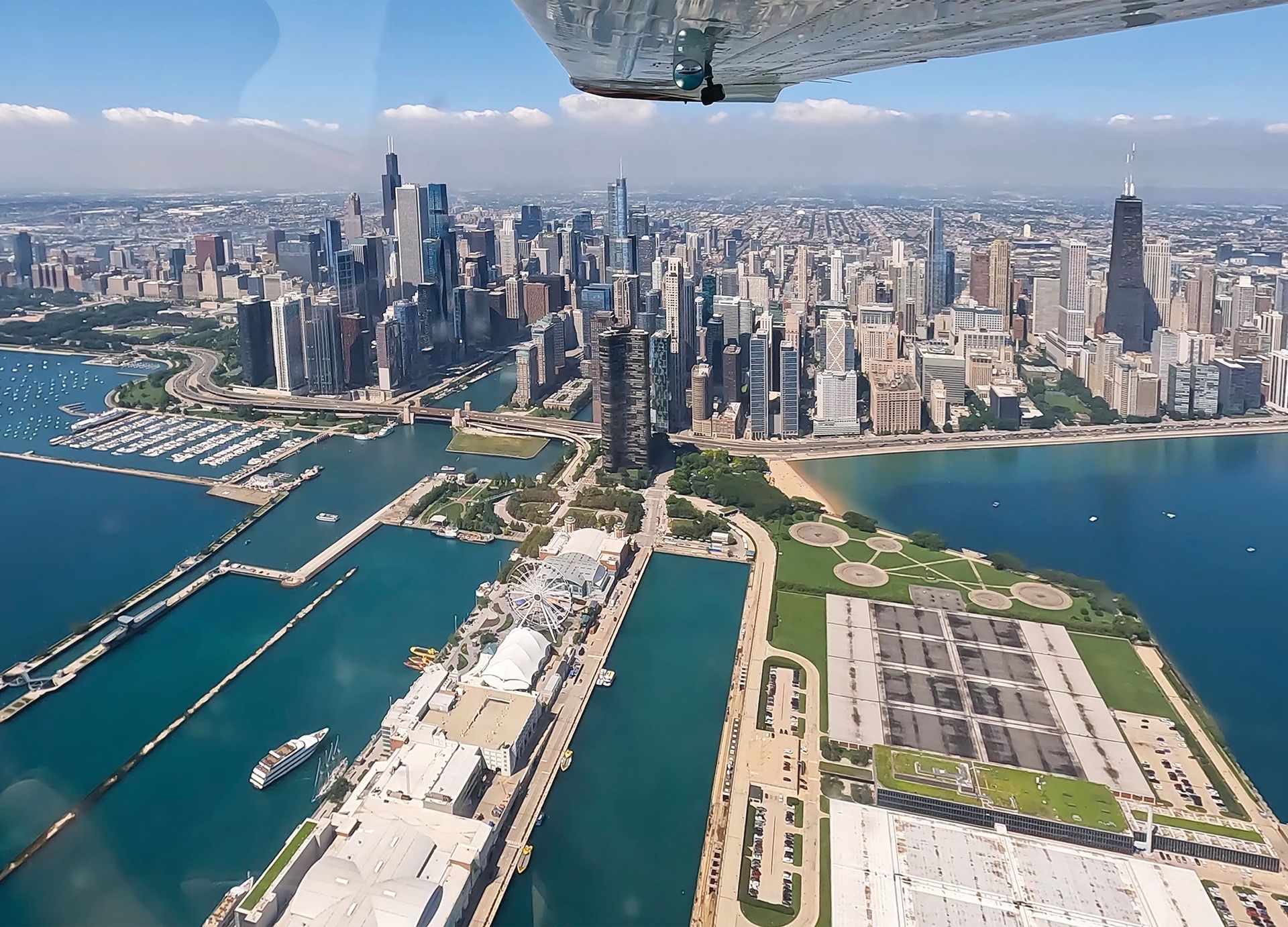 Aerial view of a waterfront city skyline with marinas, blue water, and a large green park peninsula