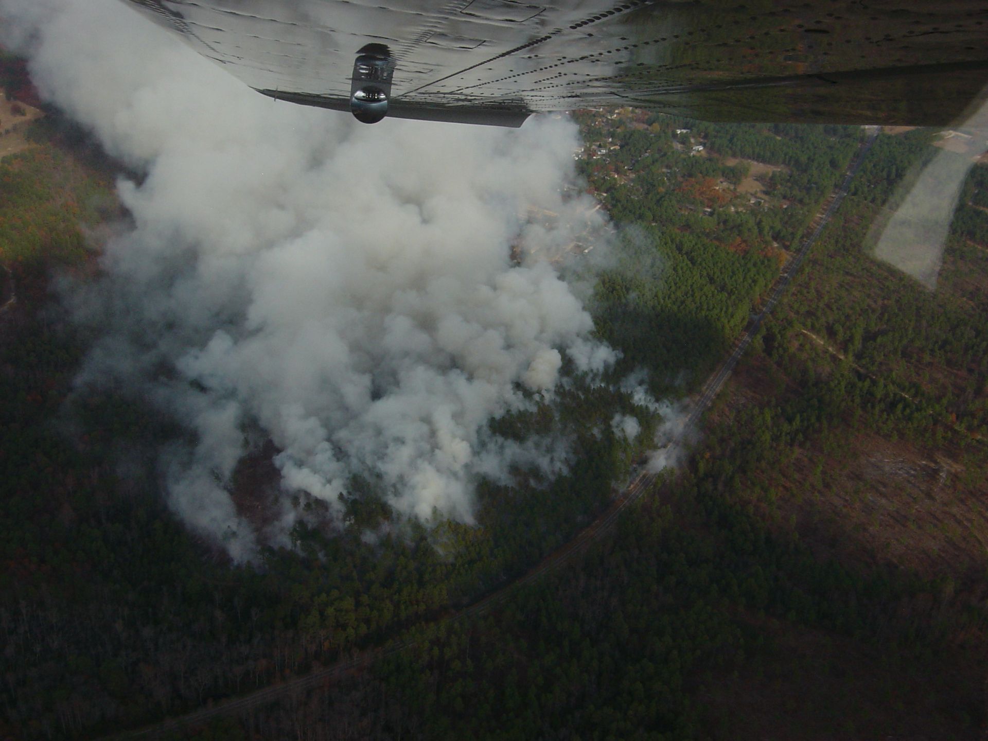 Aircraft flying over a smoky wildfire with a large plume over forested land
