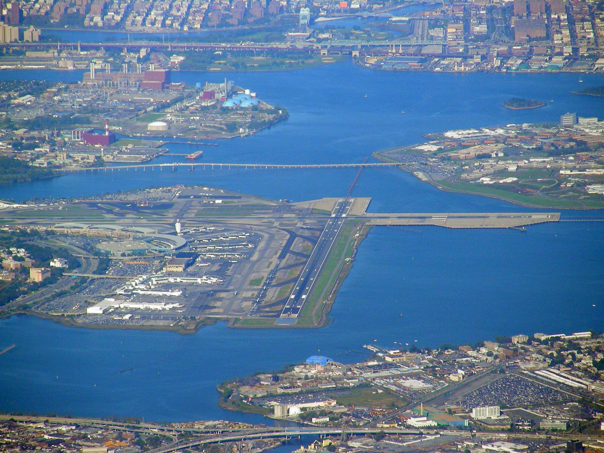Aerial view of an airport runway beside a blue waterway and urban coastline
