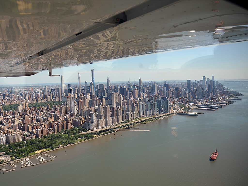 Aerial view of Manhattan skyline along the waterfront, seen from an airplane wing over the river
