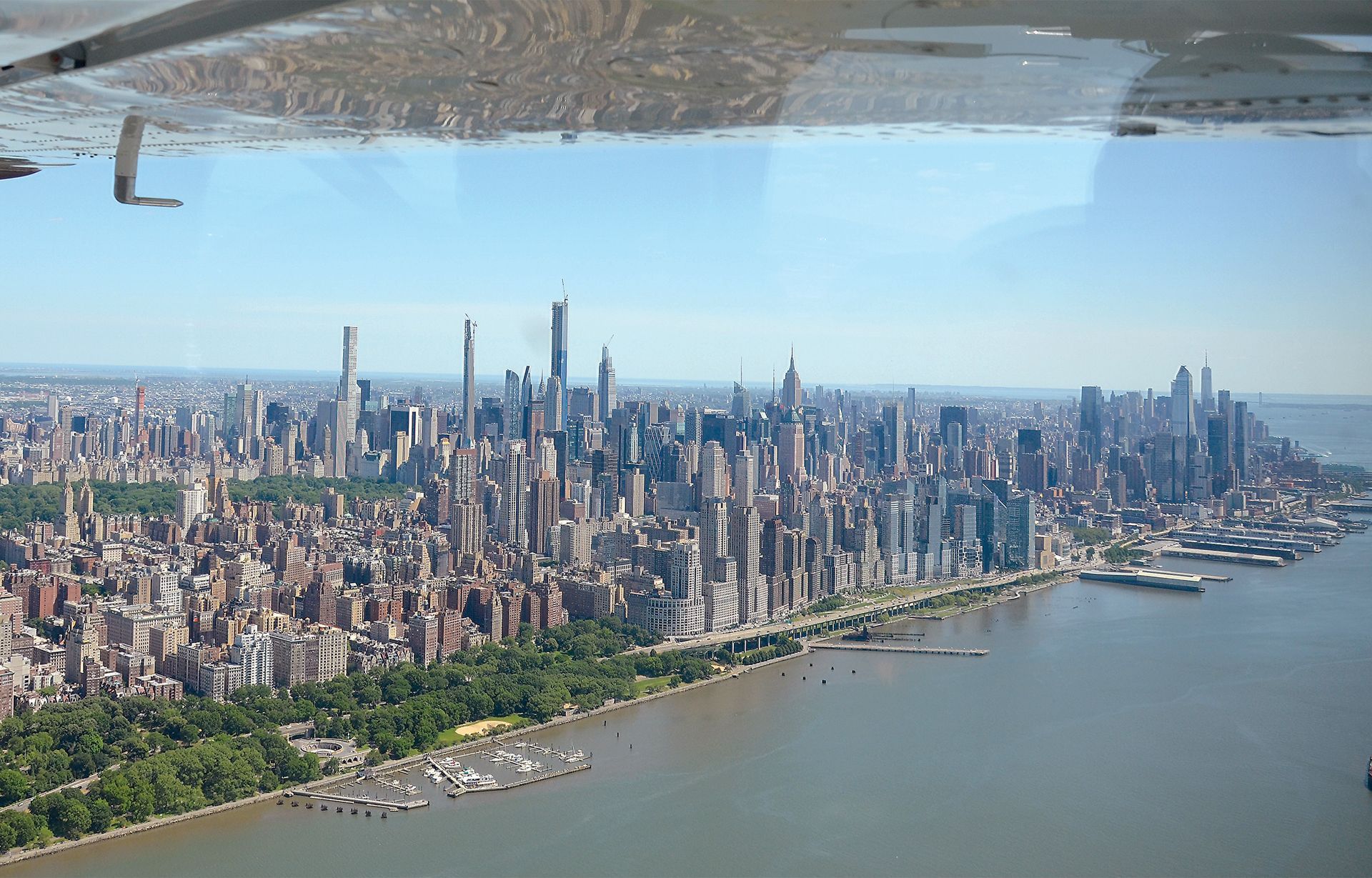 Aerial view of the New York City skyline from a plane window, featuring skyscrapers along the Hudson River waterfront.
