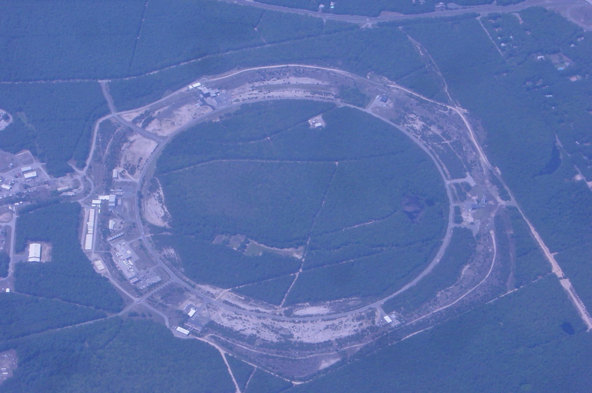 Aerial view of a large circular stadium or racetrack surrounded by forest and roads.