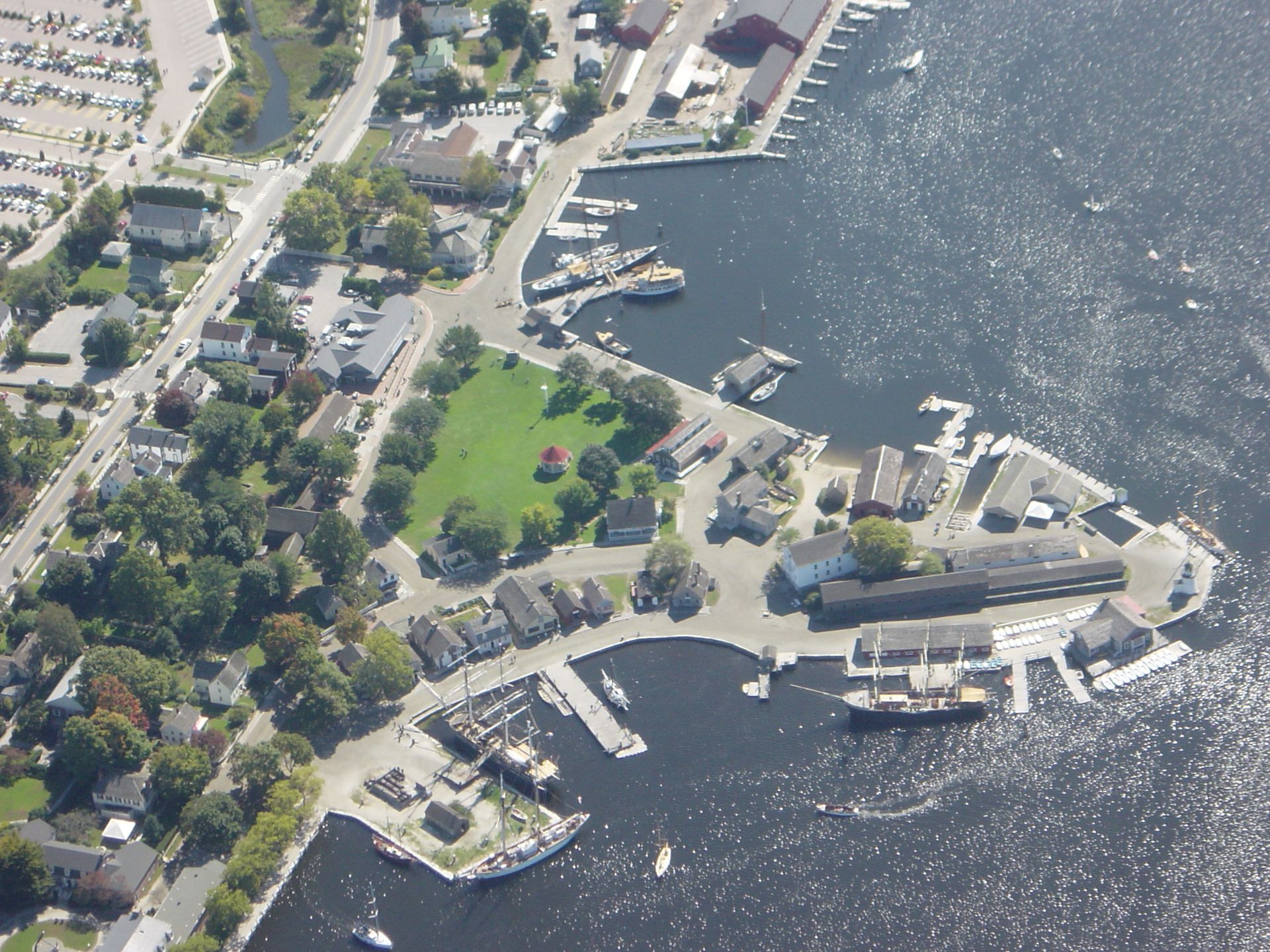 Aerial view of a waterfront harbor with docks, boats, and houses along a shoreline park.