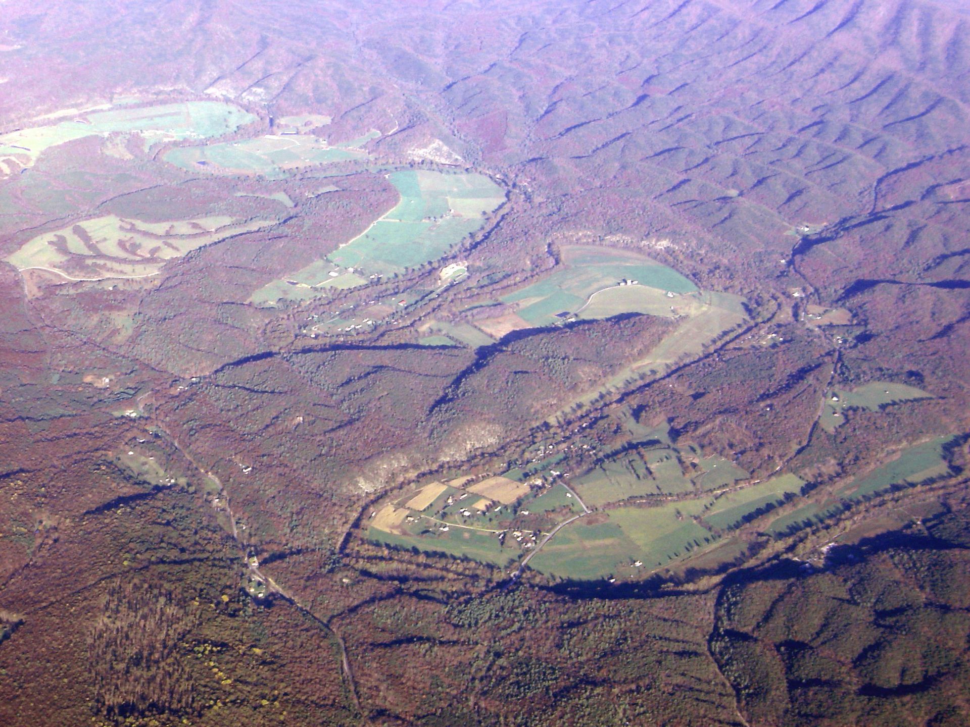 Aerial view of a brown mountainous landscape with green fields and pale turquoise ponds or lakes