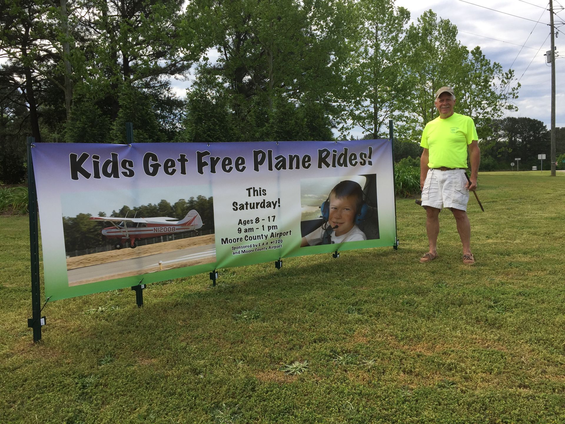 A person stands next to a banner in a grassy field that says, 