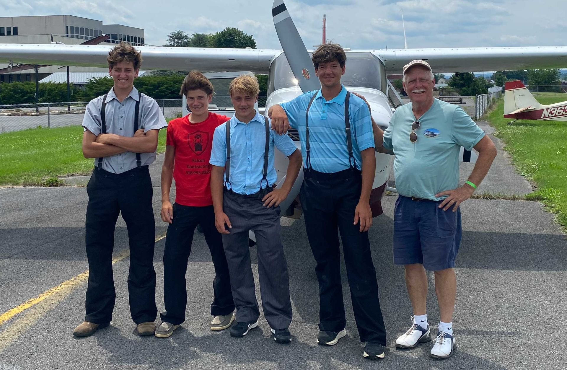 Five people stand in front of a small airplane on a tarmac, smiling at the camera.