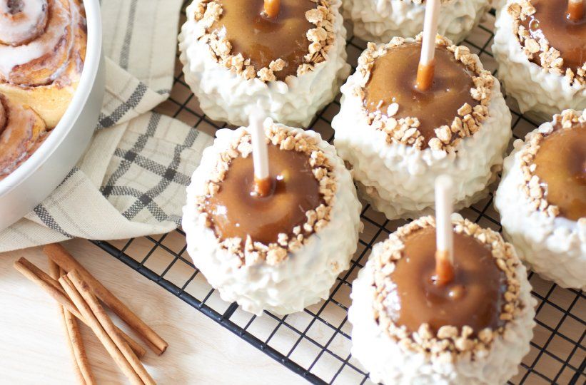 Caramel apple desserts with sticks and coconut coating on a cooling rack, with cinnamon sticks nearby