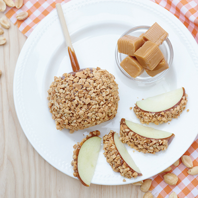 Caramel popcorn ball and caramel candies on a white plate with sliced apple wedges