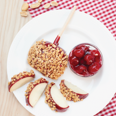 Caramel apple slices on sticks with nut coating, served with cherry topping on a white plate