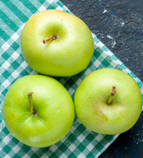 Three green apples on a green-and-white checkered cloth over a dark surface.
