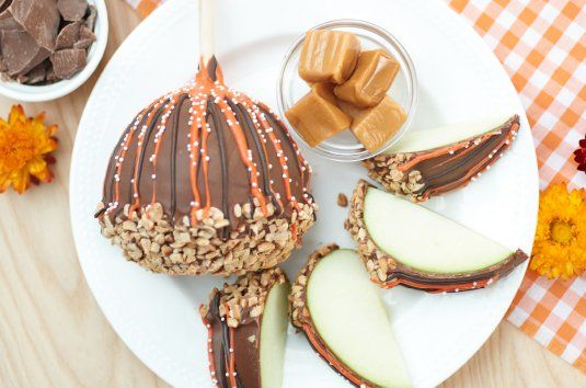 Chocolate-dipped caramel apple slices on a white plate with candy corn and autumn decor