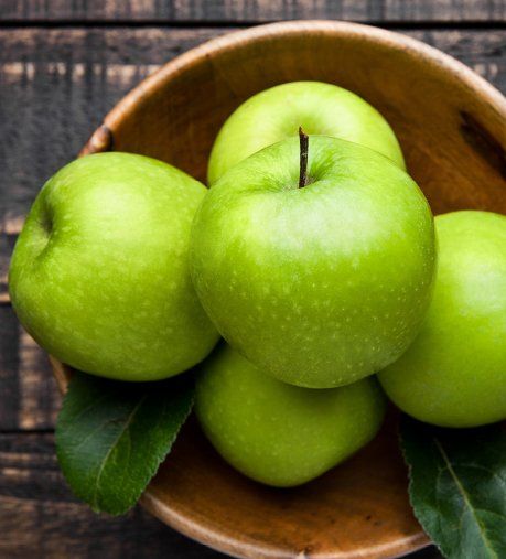 Green apples piled in a wooden bowl with leaves