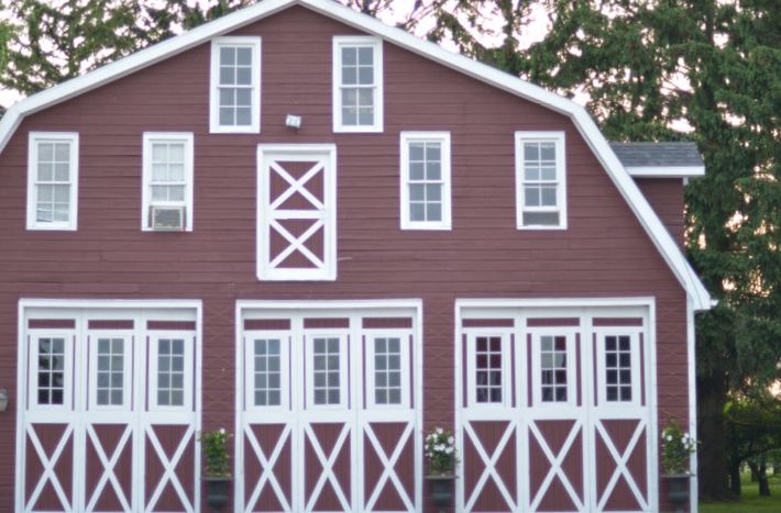 Red barn with white trim and X-pattern doors, shown front-on among trees.