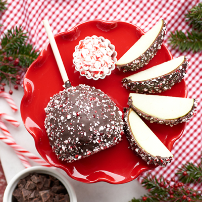 Red candy apples on a scalloped red plate, with chocolate, coconut, and white-chocolate coatings
