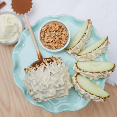 Caramel apple on blue plate with oats, apple slices, and whipped cream in a white bowl